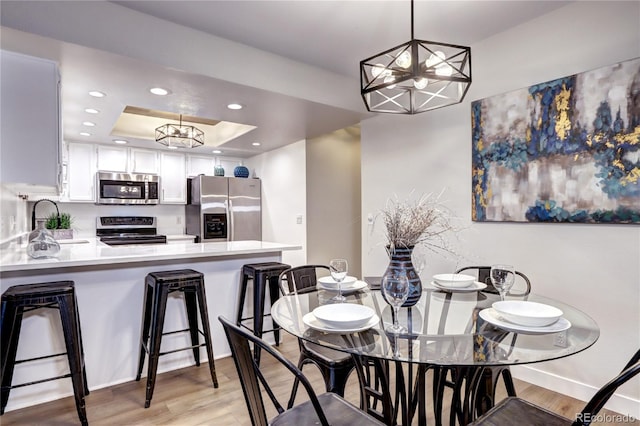 dining space featuring an inviting chandelier, a tray ceiling, light hardwood / wood-style floors, and sink