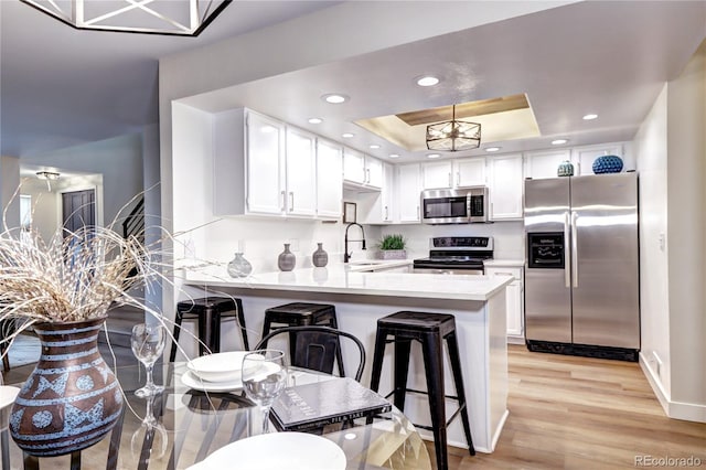 kitchen with a kitchen bar, white cabinetry, appliances with stainless steel finishes, a tray ceiling, and kitchen peninsula