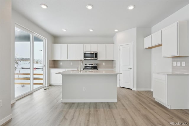 kitchen featuring white cabinetry, tasteful backsplash, light hardwood / wood-style flooring, appliances with stainless steel finishes, and an island with sink