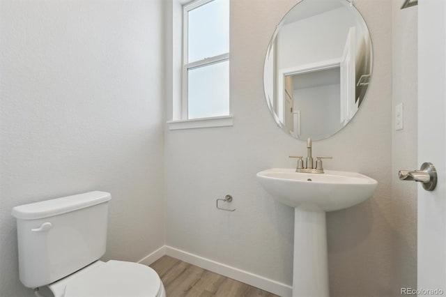 half bathroom with wood finished floors, toilet, and baseboards