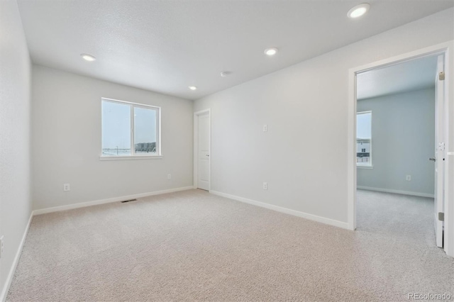 empty room with recessed lighting, light colored carpet, visible vents, and baseboards