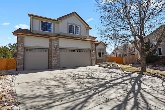 traditional-style home with brick siding, fence, an attached garage, and stucco siding