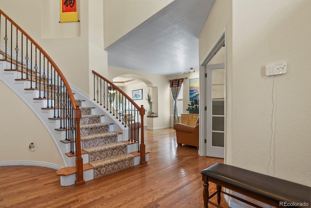 staircase with arched walkways, wood finished floors, a towering ceiling, and baseboards