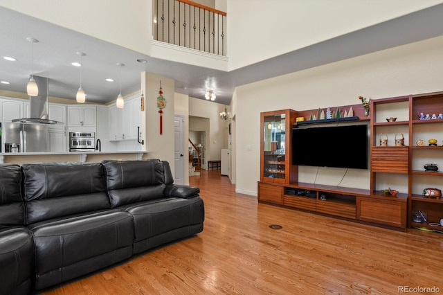 living area featuring baseboards, a towering ceiling, stairs, light wood-type flooring, and recessed lighting