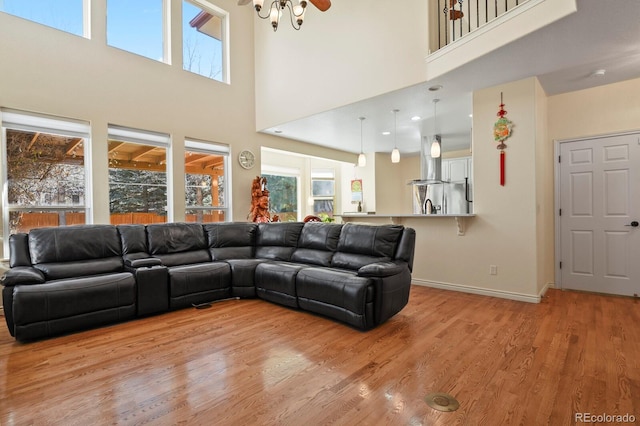 living area with a high ceiling, plenty of natural light, light wood-style flooring, and baseboards