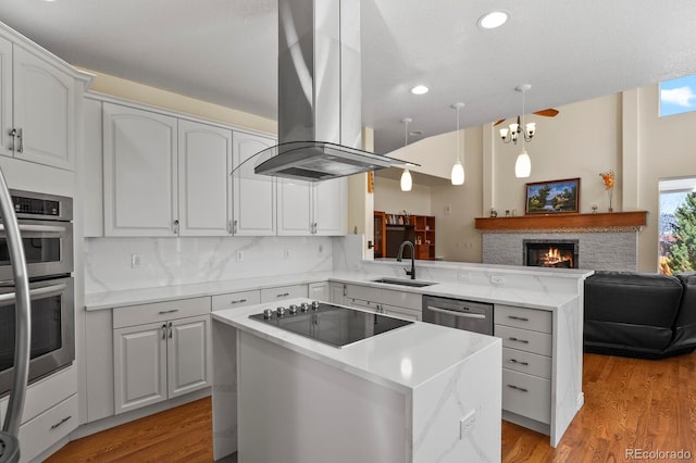 kitchen featuring appliances with stainless steel finishes, a center island, a peninsula, island exhaust hood, and a sink