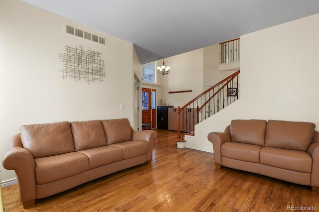 living room featuring visible vents, wood finished floors, a high ceiling, stairs, and a chandelier