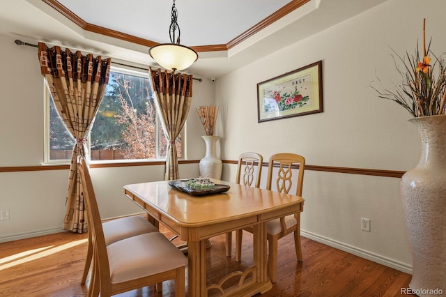 dining area with a tray ceiling, crown molding, baseboards, and wood finished floors