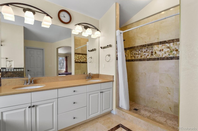 bathroom with a tile shower, double vanity, and a sink