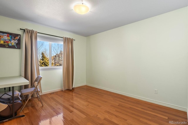 home office featuring light wood-style flooring, baseboards, and a textured ceiling