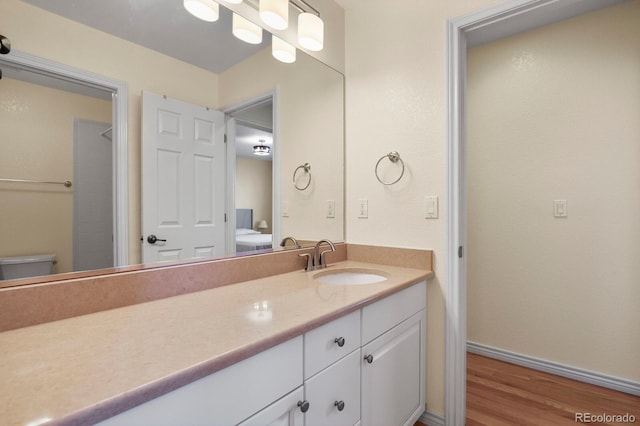 bathroom with ensuite bathroom, toilet, wood finished floors, vanity, and baseboards