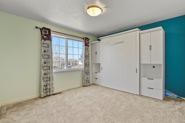 unfurnished bedroom with a textured ceiling, visible vents, baseboards, a closet, and carpet