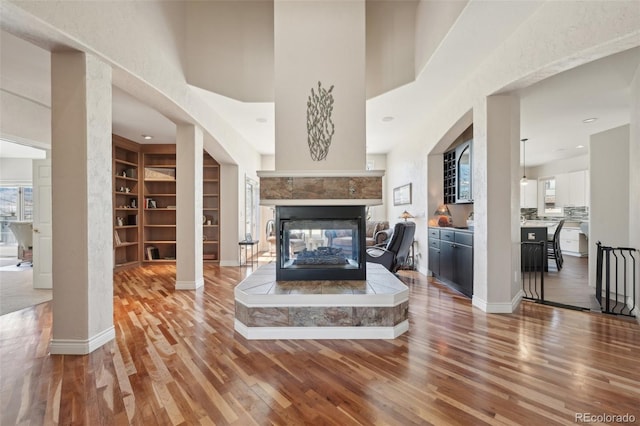 living room featuring a multi sided fireplace, built in shelves, wood finished floors, baseboards, and recessed lighting