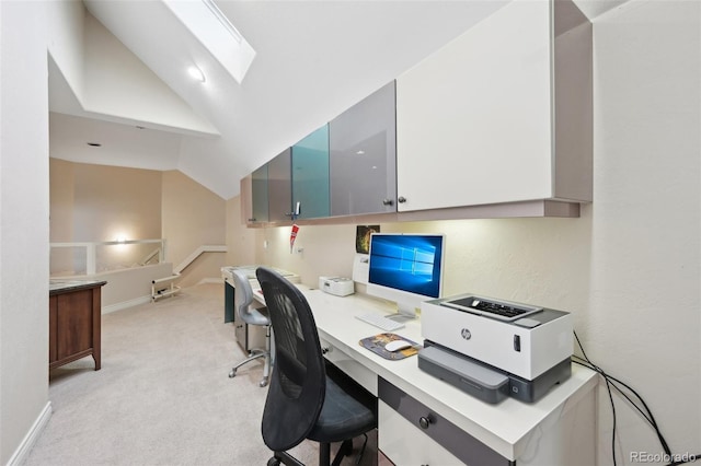 home office with baseboards, lofted ceiling with skylight, built in desk, and light colored carpet