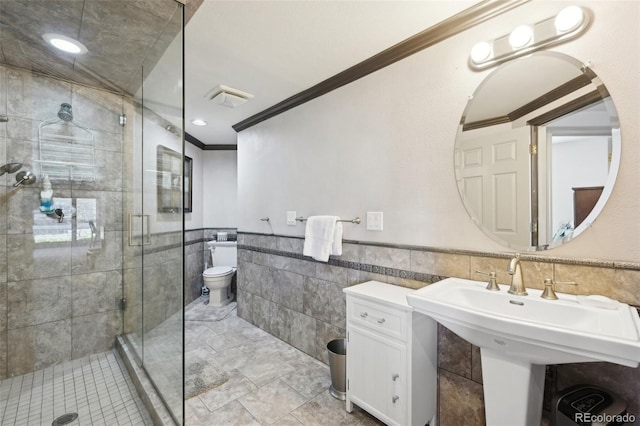 bathroom featuring crown molding, wainscoting, toilet, tile walls, and a shower stall