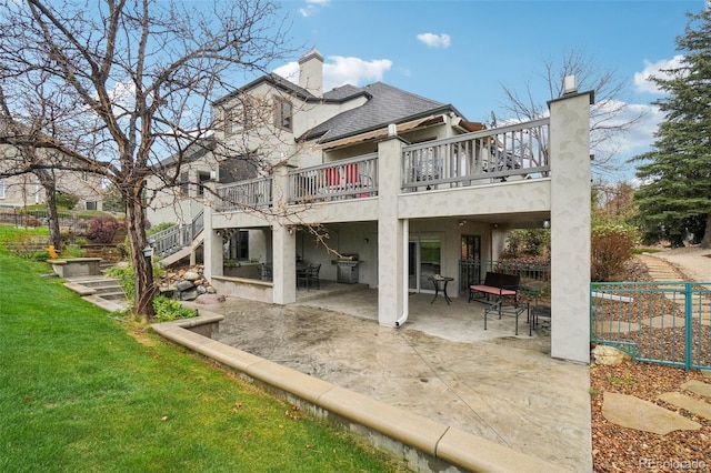 back of house featuring stairs, a shingled roof, a chimney, a lawn, and a patio
