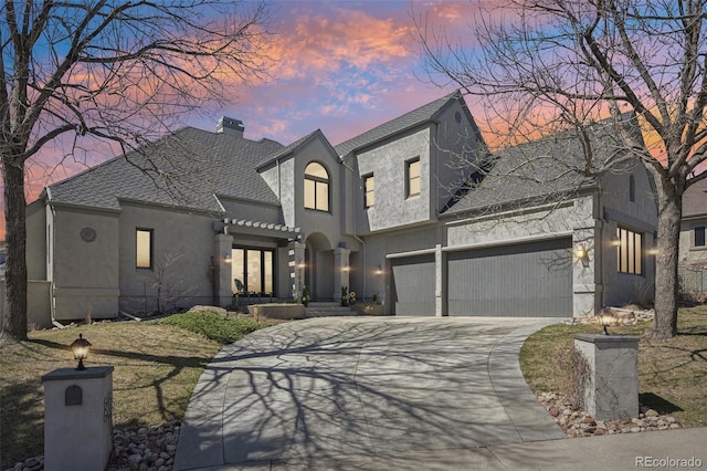 french country style house featuring roof with shingles, a garage, stucco siding, a chimney, and concrete driveway