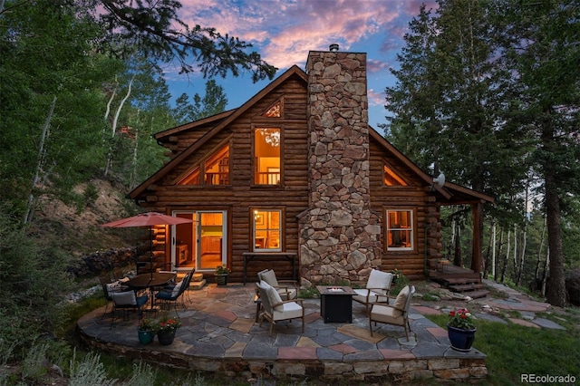80 Spruce Ct, Evergreen, CO 80439 - back of property at dusk featuring log siding, a chimney, a patio area, and an outdoor fire pit