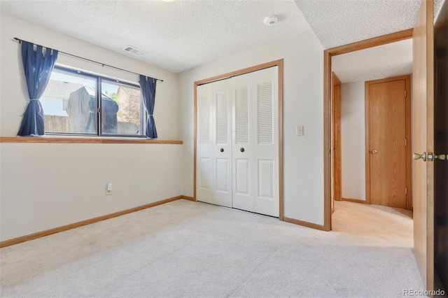 unfurnished bedroom with a closet, a textured ceiling, carpet, visible vents, and baseboards