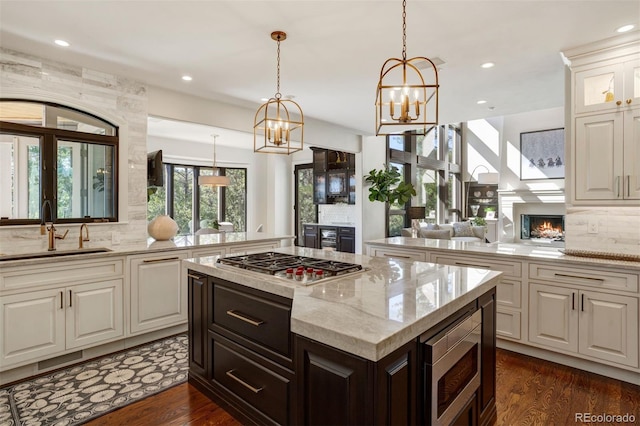 kitchen featuring pendant lighting, light stone counters, dark wood-type flooring, sink, and appliances with stainless steel finishes