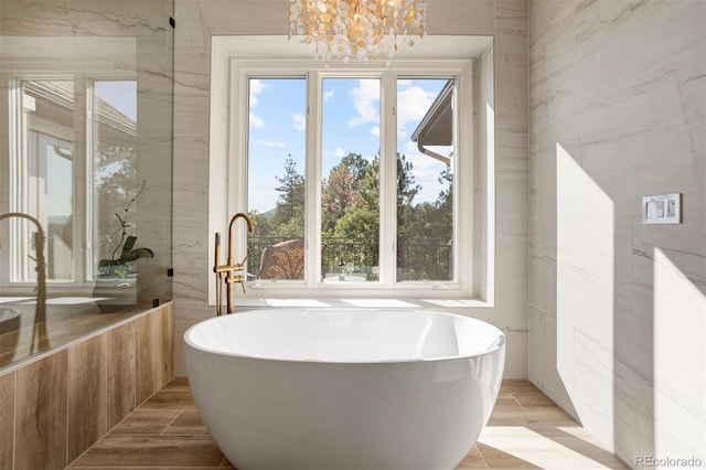 bathroom featuring a notable chandelier, a tub to relax in, and tile walls