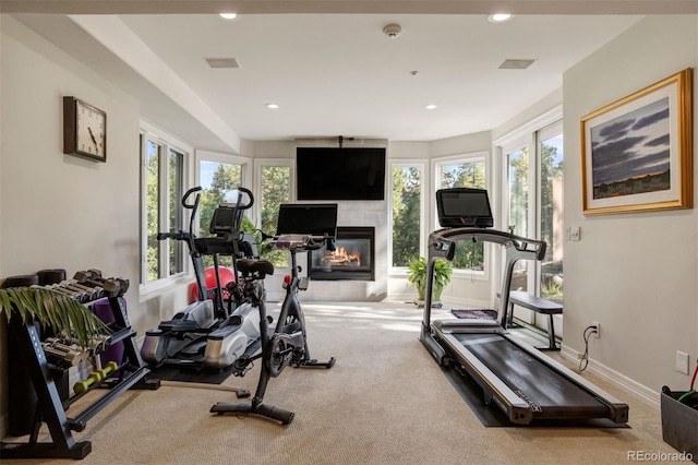 exercise room with light colored carpet, a fireplace, and plenty of natural light