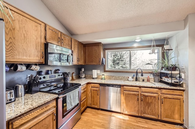 kitchen with stainless steel appliances, a sink, light wood-style flooring, a textured ceiling, and lofted ceiling