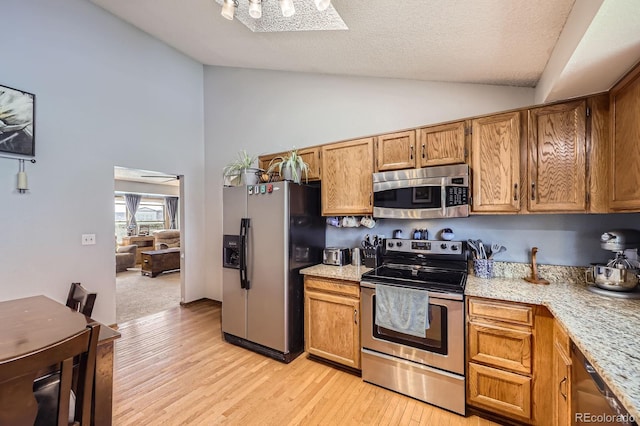 kitchen featuring appliances with stainless steel finishes, light wood-type flooring, brown cabinetry, and high vaulted ceiling
