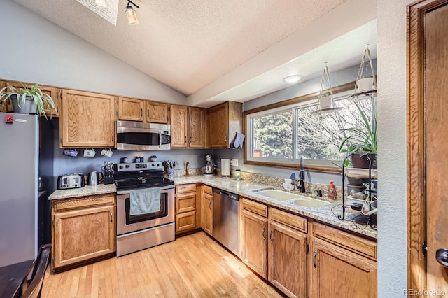 kitchen featuring stainless steel appliances, a sink, a textured ceiling, lofted ceiling, and light wood-style floors