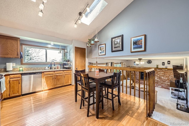dining area featuring rail lighting, light wood-type flooring, a skylight, a textured ceiling, and high vaulted ceiling