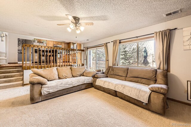 living area featuring a textured ceiling, a ceiling fan, carpet, stairway, and baseboards