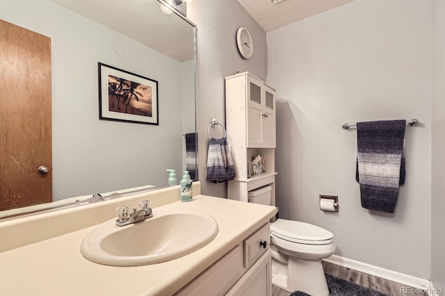bathroom with vanity, toilet, wood finished floors, and baseboards
