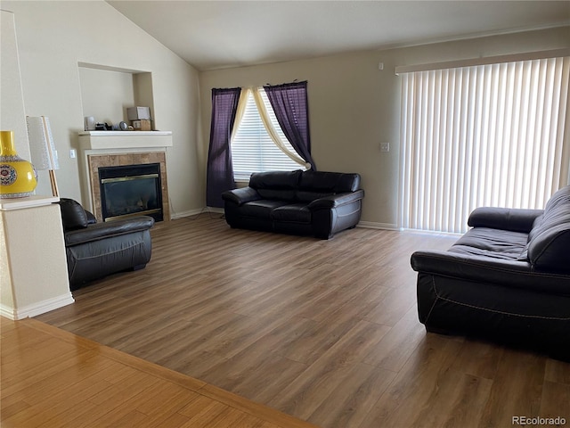 living area featuring wood finished floors, baseboards, vaulted ceiling, and a tile fireplace