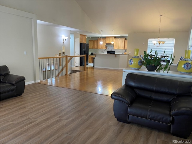 living room with high vaulted ceiling, a notable chandelier, light wood-type flooring, and baseboards