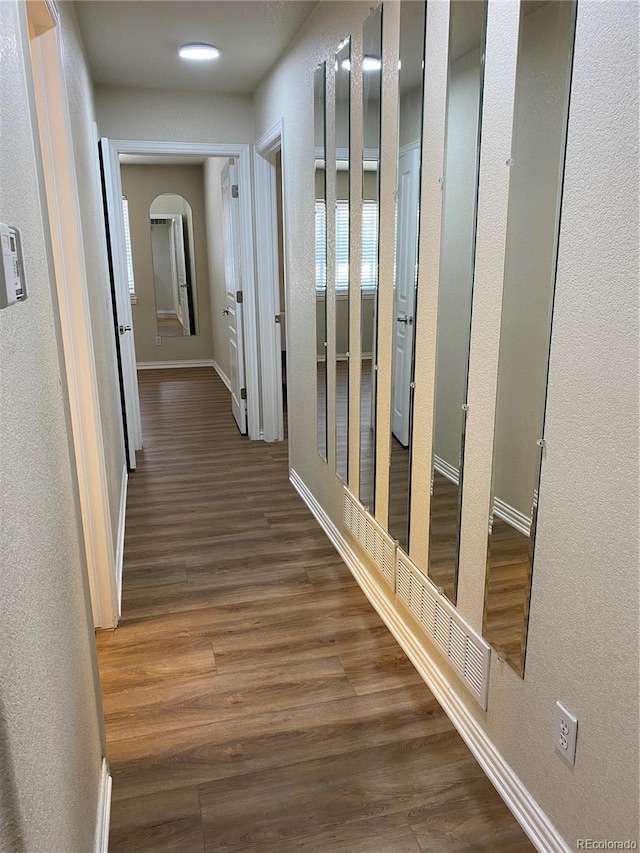 hallway featuring arched walkways, wood finished floors, a textured wall, and baseboards