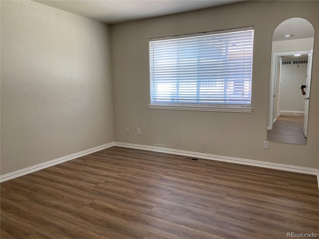empty room featuring arched walkways, baseboards, dark wood finished floors, and visible vents