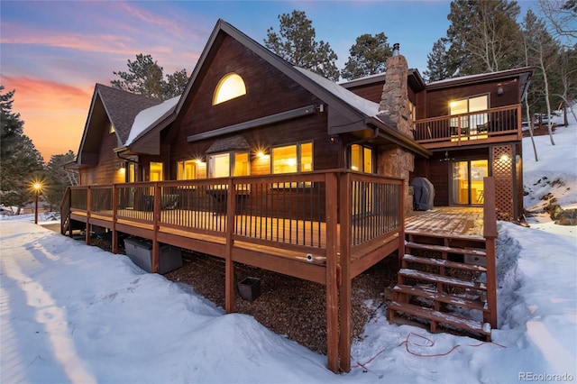 snow covered rear of property featuring a wooden deck and a balcony