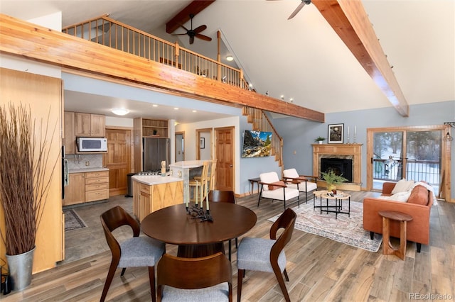 dining room featuring beam ceiling, high vaulted ceiling, hardwood / wood-style flooring, ceiling fan, and a fireplace