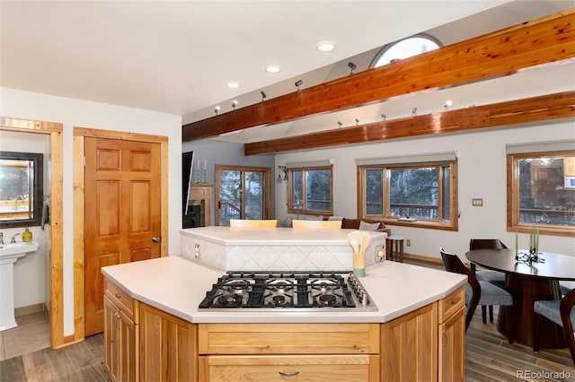 kitchen with gas cooktop, plenty of natural light, dark hardwood / wood-style flooring, a kitchen island, and beamed ceiling