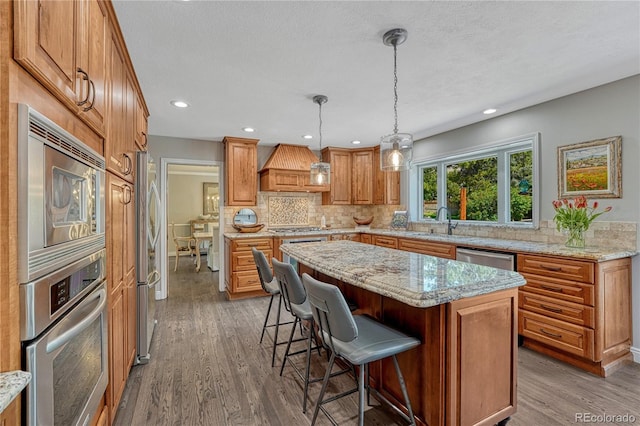 10289 E Berry Dr, Greenwood Village, CO 80111 - kitchen featuring stainless steel appliances, premium range hood, tasteful backsplash, a kitchen bar, and wood finished floors