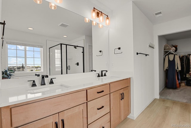 7325 S Waterloo Way, Aurora, CO 80016 - bathroom featuring wood finished floors, a shower stall, double vanity, a walk in closet, and baseboards