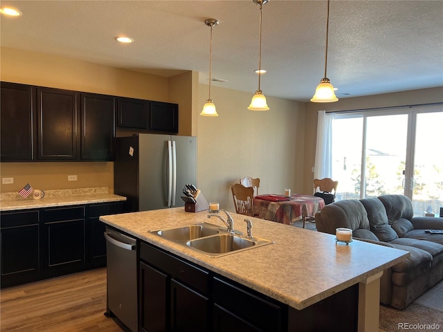 kitchen with sink, decorative light fixtures, a center island with sink, a textured ceiling, and stainless steel appliances