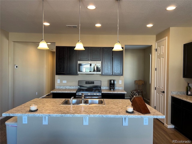 kitchen featuring a center island with sink, stainless steel appliances, dark hardwood / wood-style floors, a kitchen bar, and decorative light fixtures