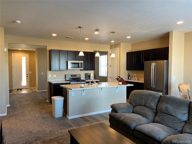 kitchen with a kitchen bar, light stone counters, hanging light fixtures, stainless steel appliances, and a kitchen island with sink