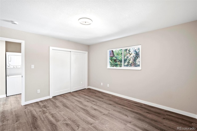 unfurnished bedroom featuring wood-type flooring, a textured ceiling, a closet, and stacked washer / dryer