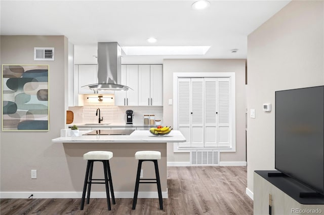 kitchen featuring sink, a kitchen bar, decorative backsplash, white cabinets, and island range hood