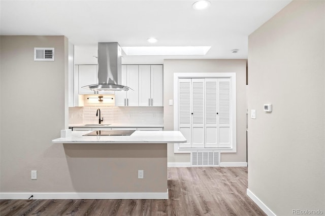 kitchen featuring island exhaust hood, tasteful backsplash, black electric cooktop, sink, and white cabinetry