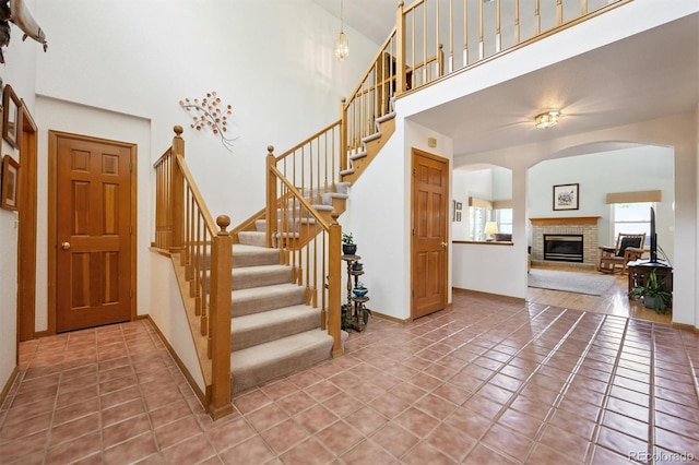 12963 W 84th Pl, Arvada, CO 80005 - stairs featuring arched walkways, a brick fireplace, a towering ceiling, and tile patterned floors