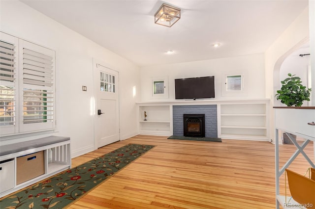 living room with built in features, light wood-type flooring, and a brick fireplace