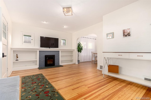 living room with a fireplace, built in features, and light wood-type flooring